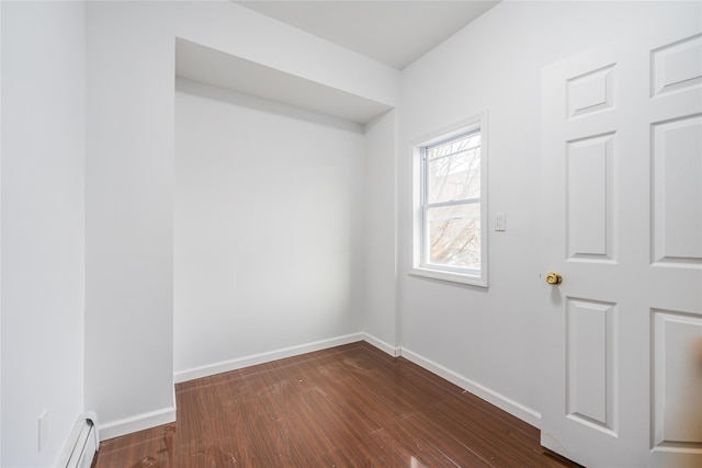 spare room featuring a baseboard heating unit, baseboards, and dark wood-style floors