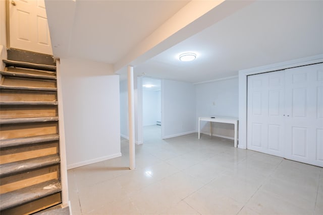 finished basement with light tile patterned floors, a baseboard radiator, stairs, and baseboards