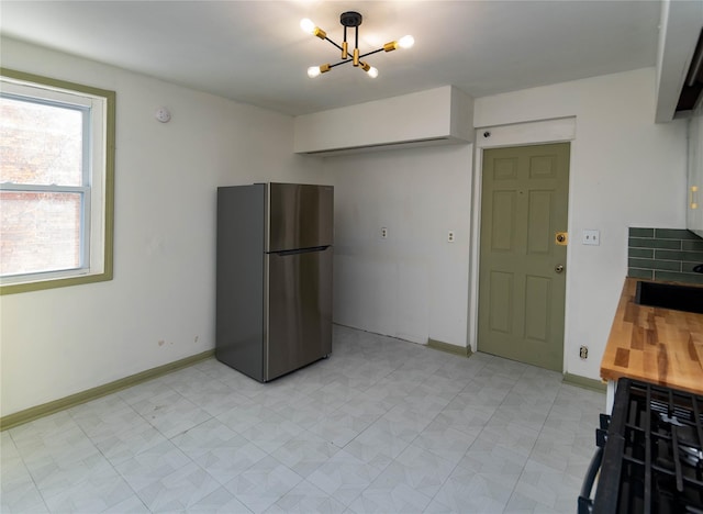 kitchen with a notable chandelier, a sink, baseboards, freestanding refrigerator, and light floors