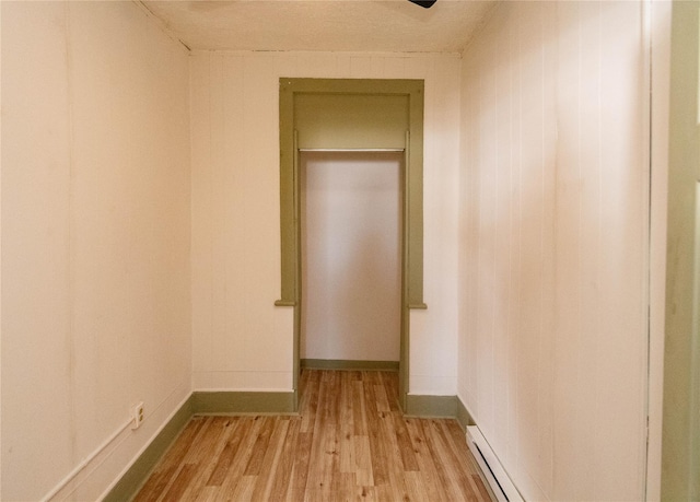 corridor with light wood-type flooring, baseboards, and baseboard heating