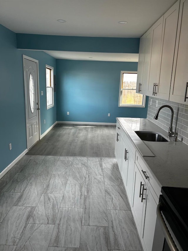 kitchen with tasteful backsplash, baseboards, white cabinets, light stone countertops, and a sink