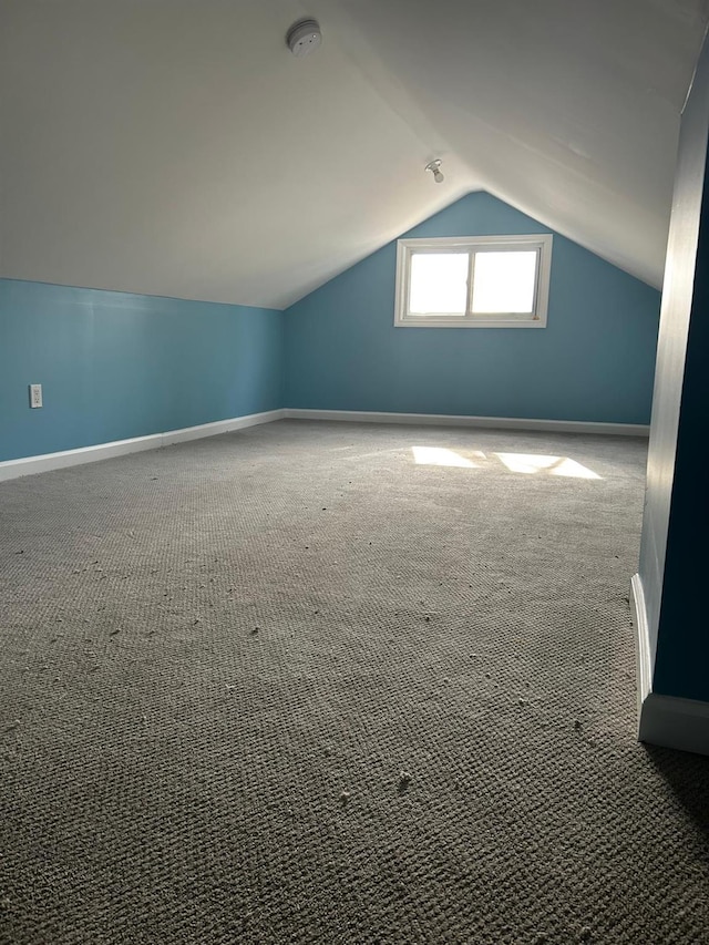 additional living space with vaulted ceiling, dark carpet, and baseboards