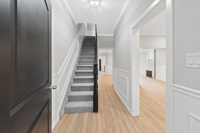 staircase with crown molding, a decorative wall, and wood finished floors