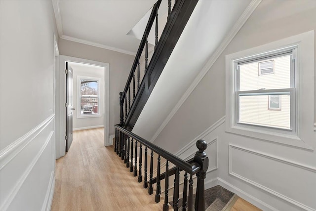 stairs with a decorative wall, wood finished floors, and crown molding