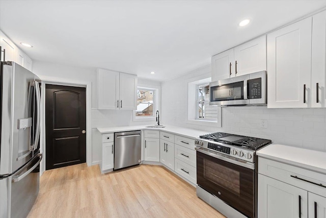 kitchen featuring light wood finished floors, stainless steel appliances, light countertops, white cabinetry, and a sink