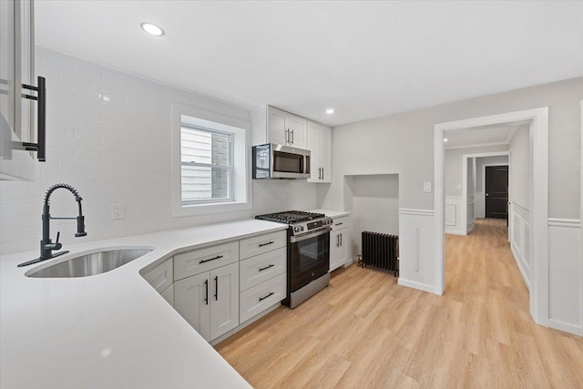 kitchen with appliances with stainless steel finishes, radiator, white cabinets, and a sink