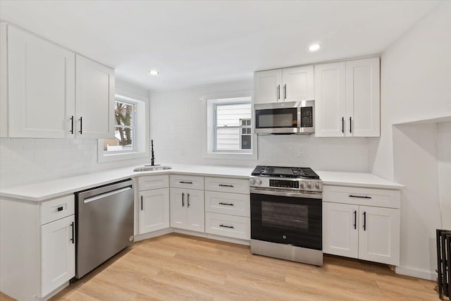 kitchen featuring stainless steel appliances, light countertops, light wood-style flooring, white cabinets, and a sink