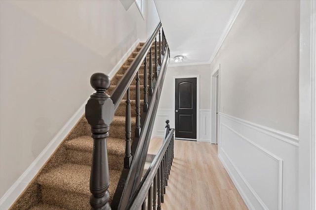 stairway with a wainscoted wall, crown molding, a decorative wall, and wood finished floors