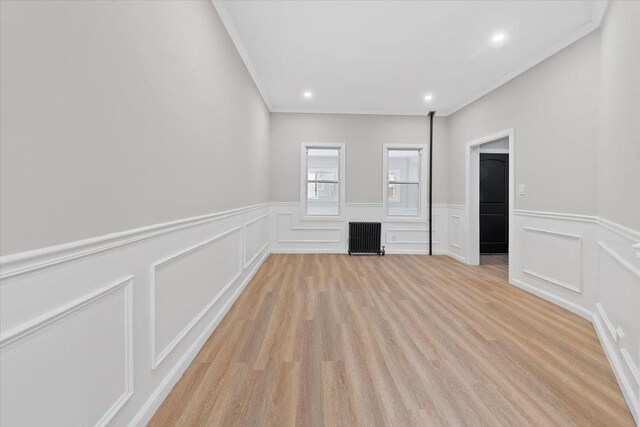 unfurnished living room with light wood-type flooring, radiator, crown molding, and recessed lighting