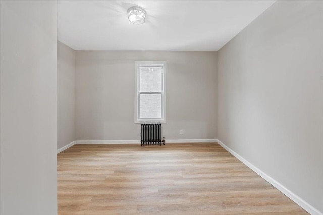 spare room featuring baseboards, light wood finished floors, and radiator heating unit