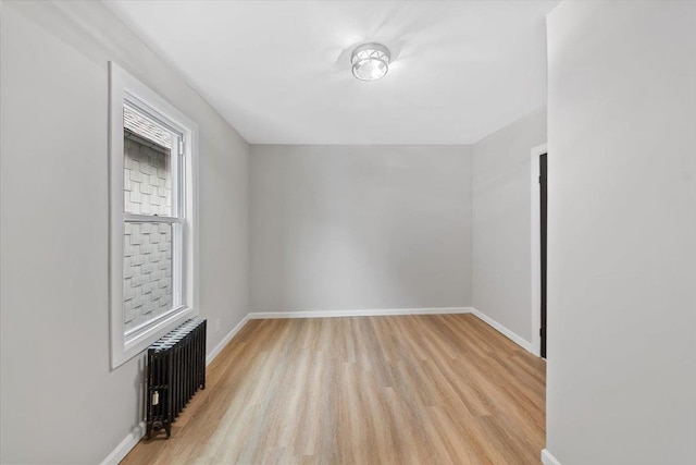 unfurnished room featuring radiator, baseboards, and light wood finished floors