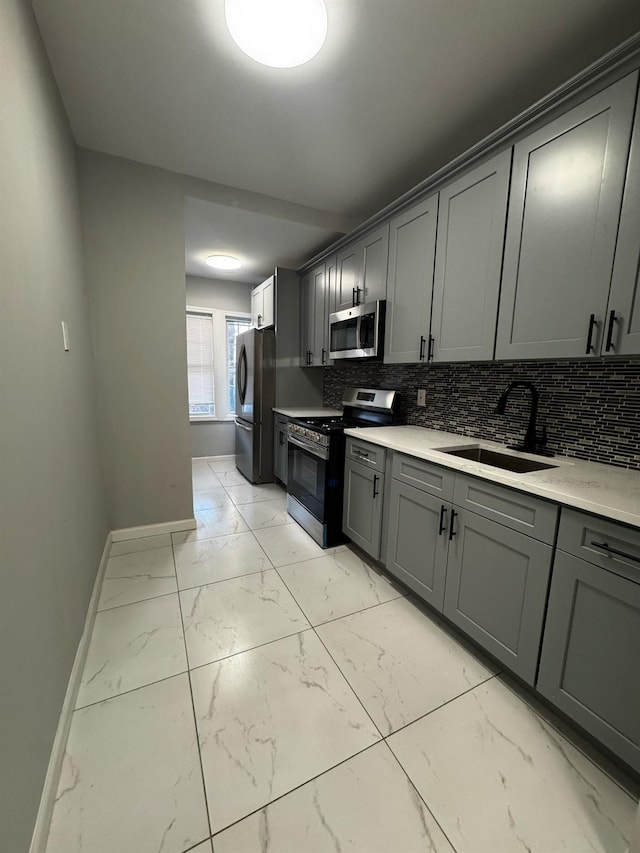 kitchen with gray cabinetry, stainless steel appliances, a sink, marble finish floor, and light countertops