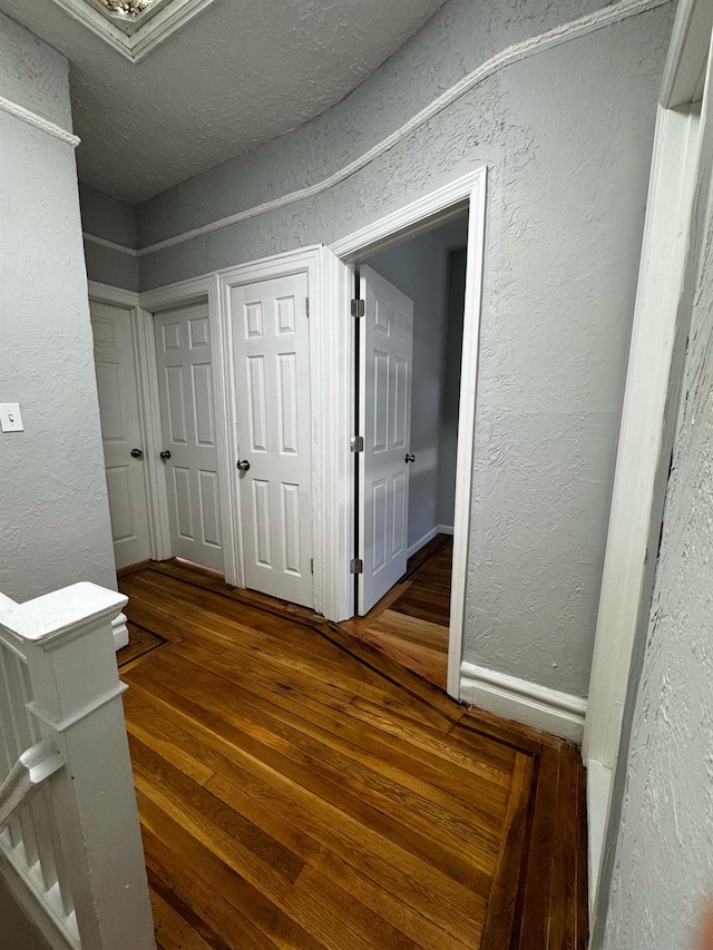 corridor featuring baseboards, dark wood finished floors, and a textured wall