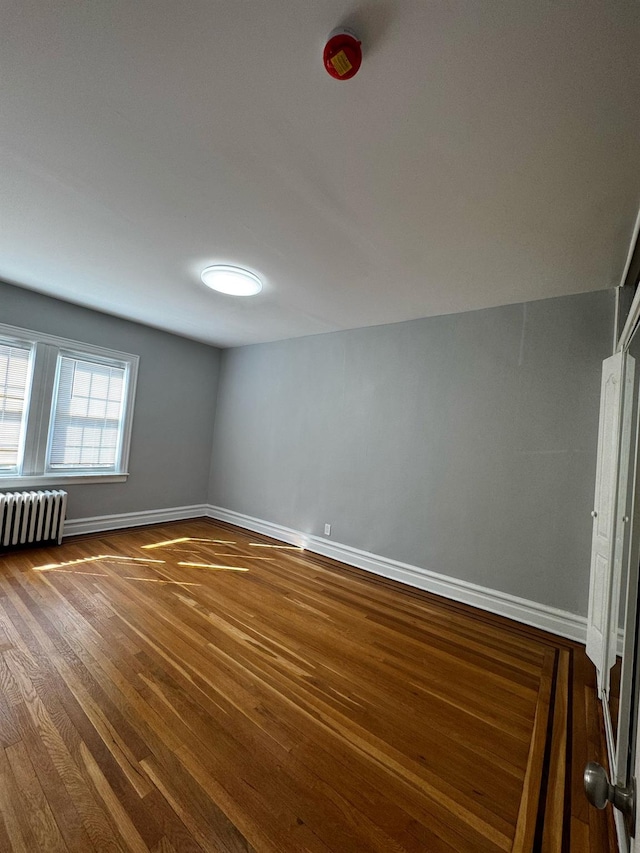 unfurnished room featuring baseboards, wood finished floors, and radiator