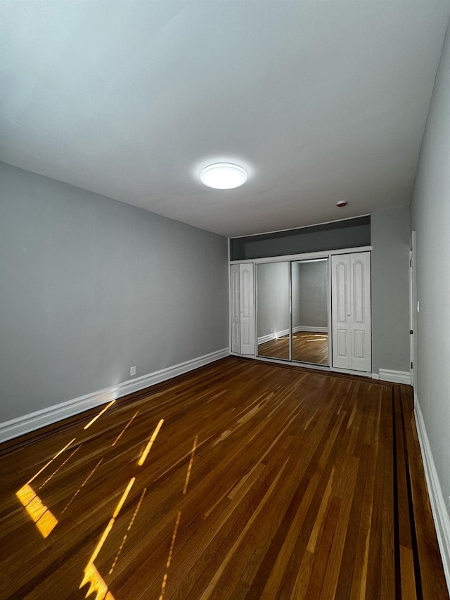 unfurnished bedroom with a closet, baseboards, and dark wood-type flooring