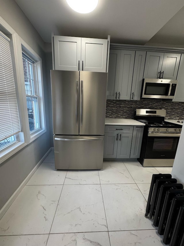 kitchen with gray cabinetry, stainless steel appliances, marble finish floor, light countertops, and decorative backsplash