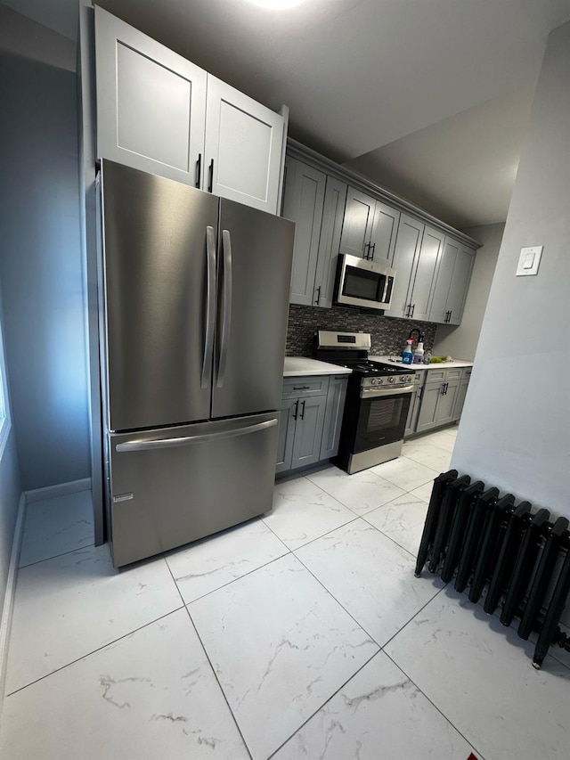 kitchen featuring marble finish floor, stainless steel appliances, tasteful backsplash, light countertops, and gray cabinetry