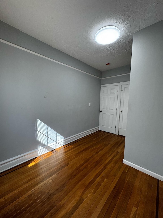 unfurnished room with a textured ceiling, dark wood-type flooring, and baseboards