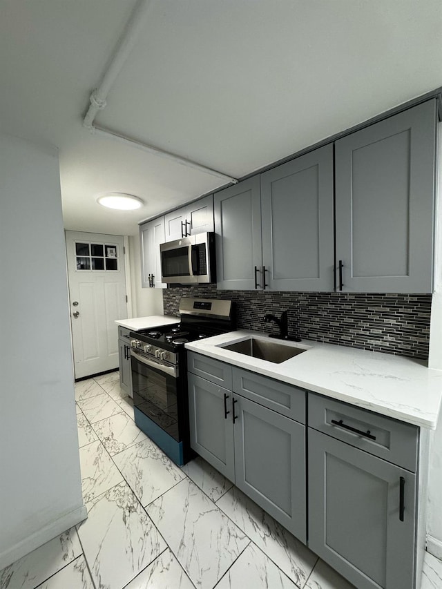 kitchen featuring marble finish floor, stainless steel appliances, a sink, and gray cabinetry