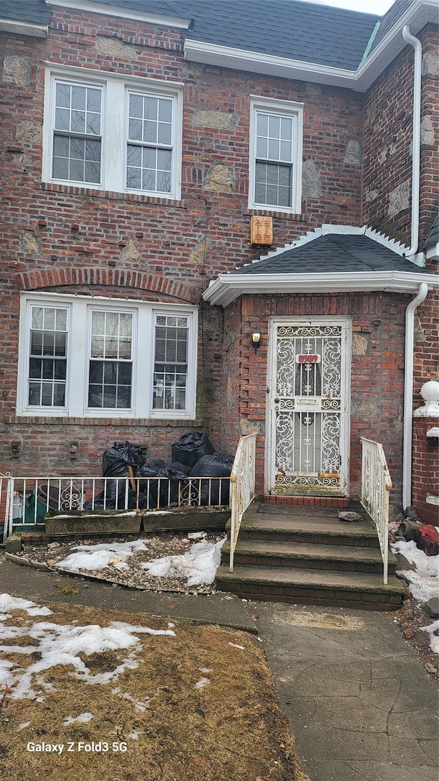 view of front facade with roof with shingles and brick siding