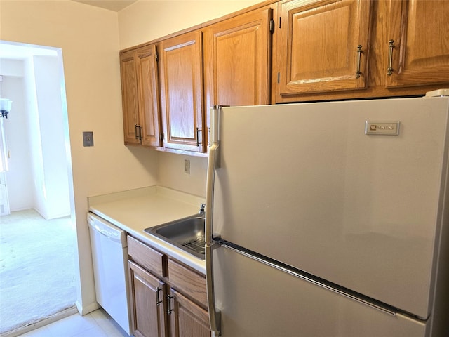 kitchen featuring brown cabinets, a sink, freestanding refrigerator, white dishwasher, and light countertops