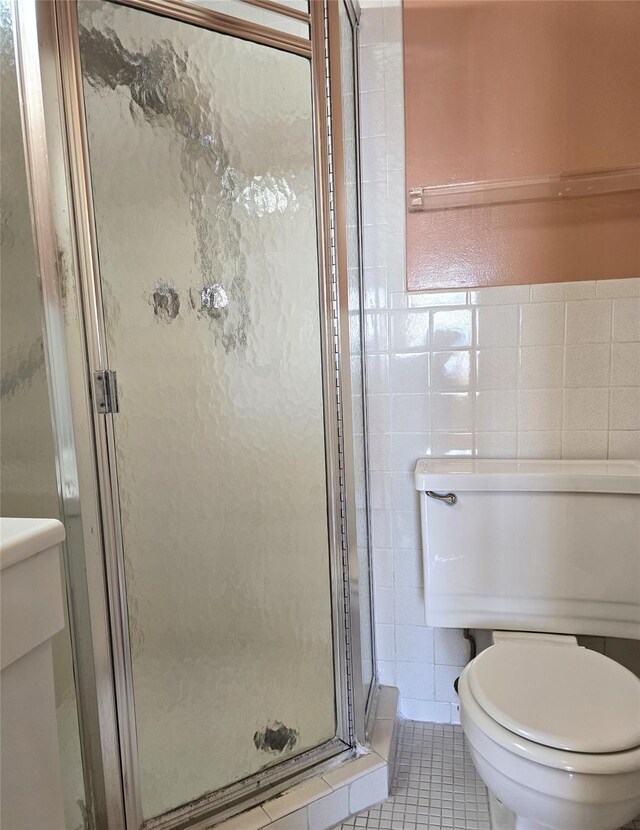 bathroom with tile patterned floors, toilet, tile walls, and a shower stall