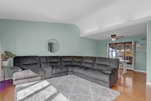 living area featuring light wood-style flooring, a ceiling fan, an AC wall unit, vaulted ceiling, and baseboards