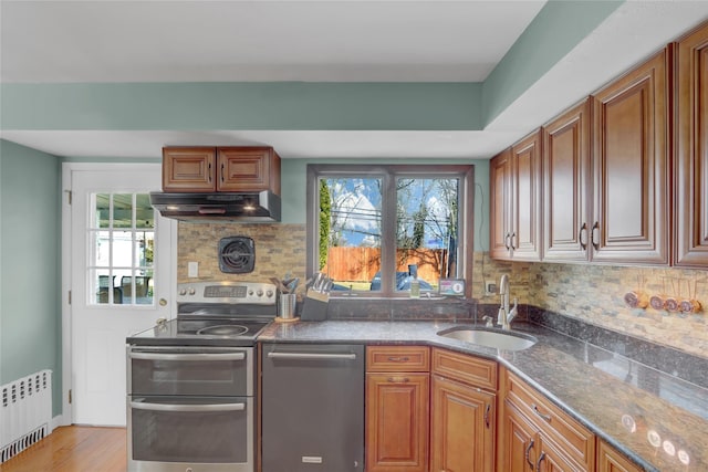 kitchen featuring radiator heating unit, appliances with stainless steel finishes, a sink, plenty of natural light, and under cabinet range hood