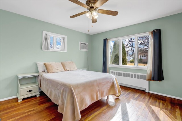 bedroom featuring radiator, multiple windows, baseboards, and hardwood / wood-style floors