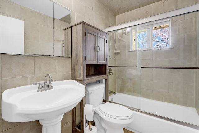 bathroom with tile walls, backsplash, toilet, combined bath / shower with glass door, and a sink