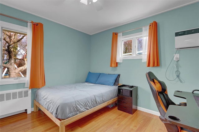 bedroom featuring a wall unit AC, radiator, a ceiling fan, wood finished floors, and baseboards