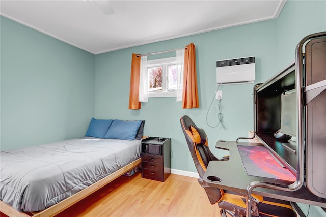 bedroom with a wall unit AC, baseboards, and wood finished floors