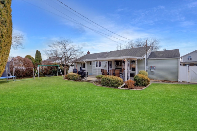 rear view of house with a trampoline, a yard, fence, and a patio