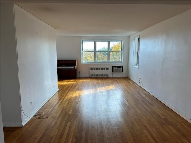unfurnished living room featuring an AC wall unit, baseboards, dark wood finished floors, and radiator heating unit