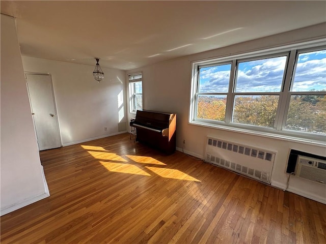 unfurnished room with radiator heating unit, baseboards, wood finished floors, and a wall mounted air conditioner