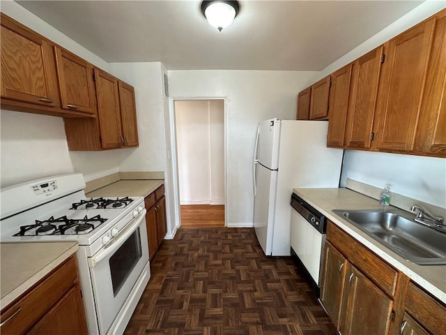 kitchen with brown cabinets, white appliances, light countertops, and a sink