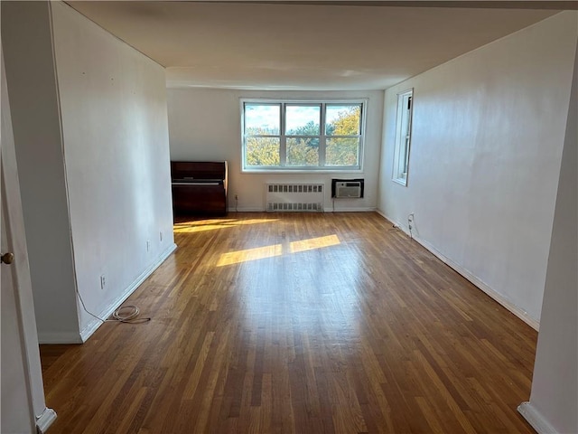unfurnished living room with radiator heating unit, baseboards, dark wood finished floors, and a wall mounted AC