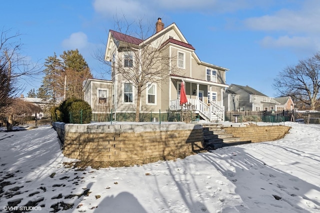 victorian home featuring covered porch, a fenced front yard, a chimney, and metal roof