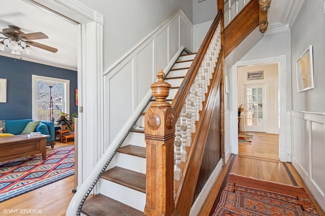 staircase with a decorative wall, wainscoting, wood finished floors, and crown molding