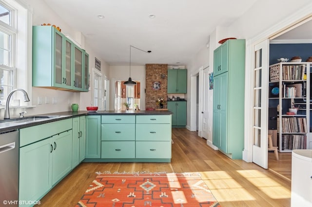 kitchen featuring green cabinetry, dishwasher, glass insert cabinets, pendant lighting, and a sink