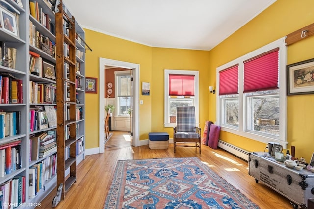 living area featuring light wood-type flooring, a baseboard radiator, baseboards, and crown molding