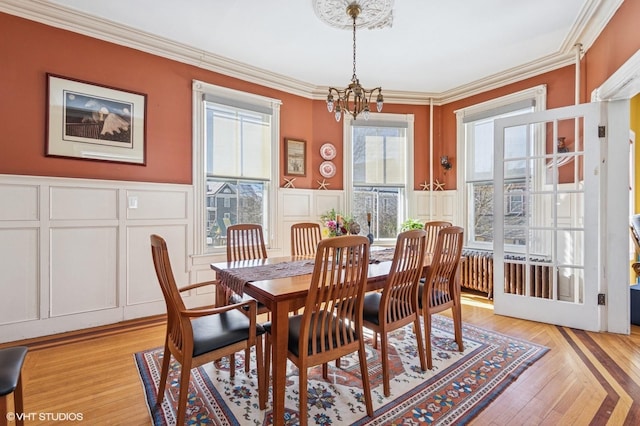 dining area featuring wainscoting, crown molding, light wood-style floors, a decorative wall, and a notable chandelier