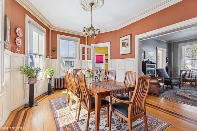 dining room featuring a wainscoted wall, crown molding, a decorative wall, light wood-style floors, and a chandelier