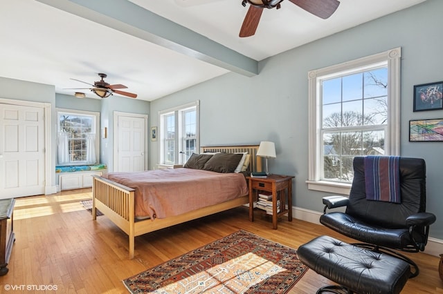 bedroom with multiple windows, beamed ceiling, baseboards, and wood finished floors