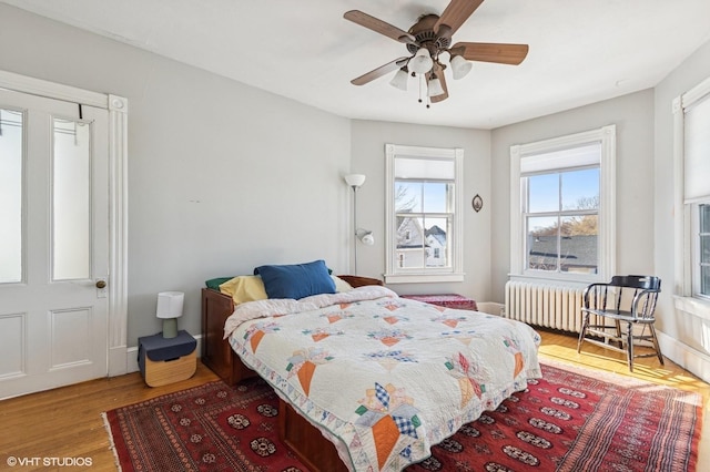 bedroom with radiator heating unit, wood finished floors, a ceiling fan, and baseboards