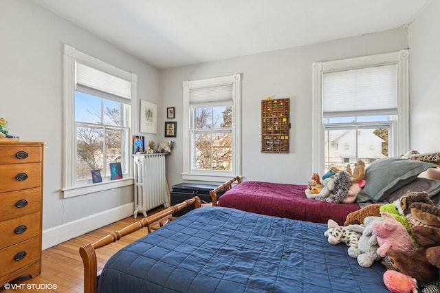 bedroom with baseboards, multiple windows, radiator heating unit, and wood finished floors