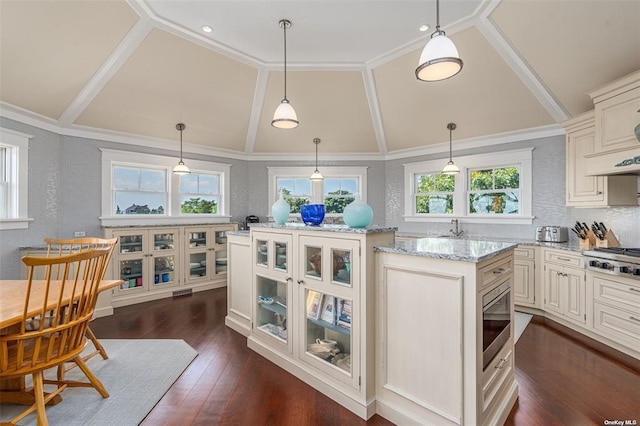 kitchen with light stone counters, decorative light fixtures, dark wood finished floors, stainless steel gas stovetop, and glass insert cabinets