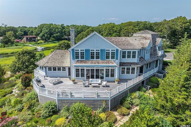 back of property with an outdoor hangout area, a chimney, a deck, and a view of trees