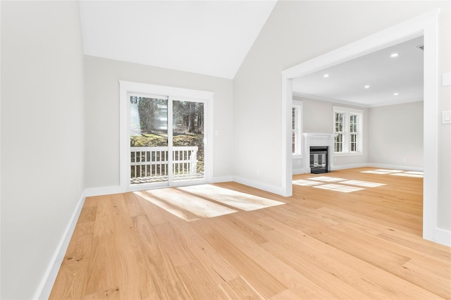 unfurnished living room with light wood-type flooring, baseboards, lofted ceiling, and a glass covered fireplace