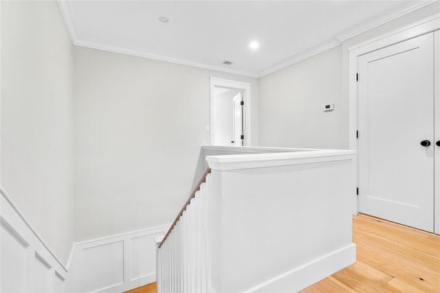 hallway featuring visible vents, an upstairs landing, a wainscoted wall, light wood-style flooring, and ornamental molding